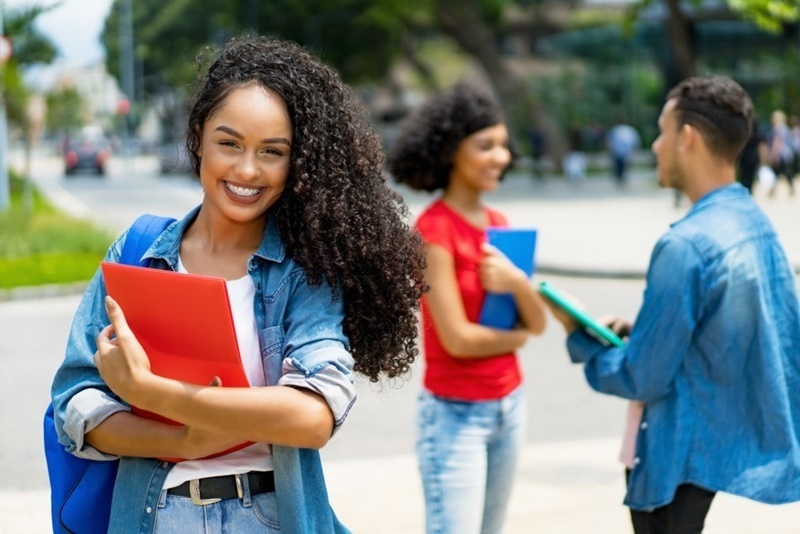 Mulher sorrindo segurando uma pasta com a imagem do VEM estudante do lado
